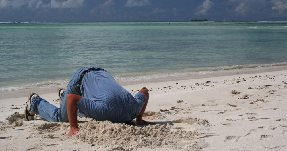 Man on beach with head in the sand.