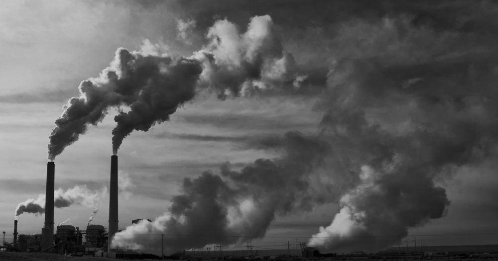black and white photo of a coal-fired power plant with two tall smokestacks releasing large plumes of smoke into the sky