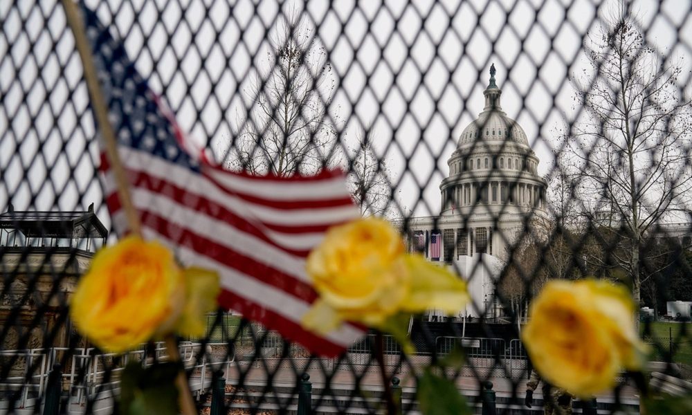 The US Capitol seen through a fence with flowers and a US flag inserted in it