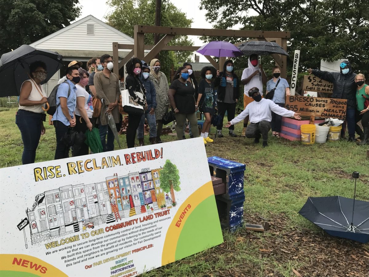 a group of people belonging to the Community Land Trust pose for a photo; many wear masks and hold umbrellas