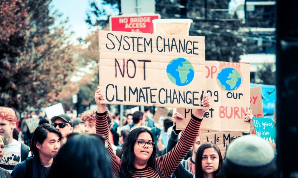 A young woman holds a sign that reads "system change, not climate change" at a youth climate strike march in Vancouver, Canada