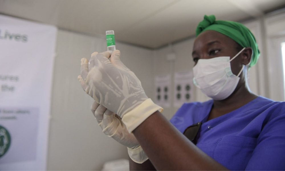 a woman wearing a head wrap, mask, and rubber medical gloves holds a vial of COVID-19 vaccine in a hospital in Mogadishu, Somalia