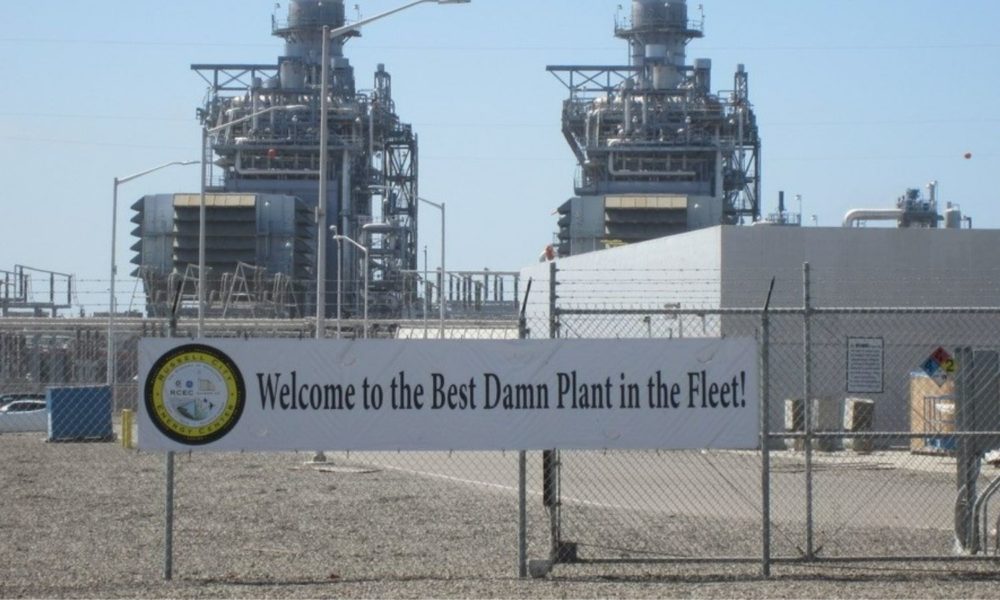 a photo of the Russell City Energy Center in Hayward, California, taken by the blog author on his tour. a sign on the chainlink fence in front of the plant reads, "welcome to the best damn plant in the fleet!"