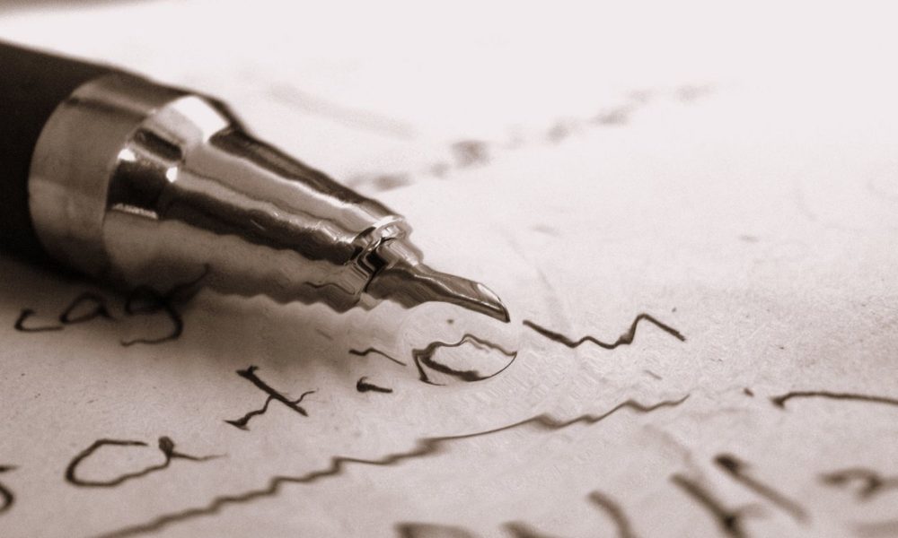a fountain pen in close-up rests on a sheet of paper with writing on it. the nib of the pen is in focus