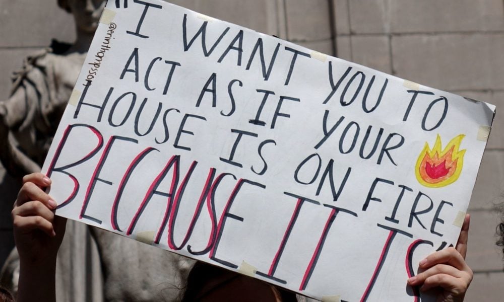 a pair of hands holds up a sign reading "I want you to act as if your house is on fire, because it is" at a youth climate protest in NYC