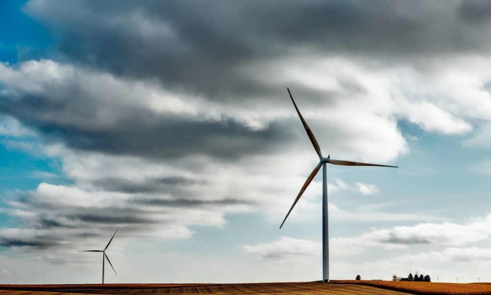 a wind farm is set against a plain with cloudy blue skies overhead