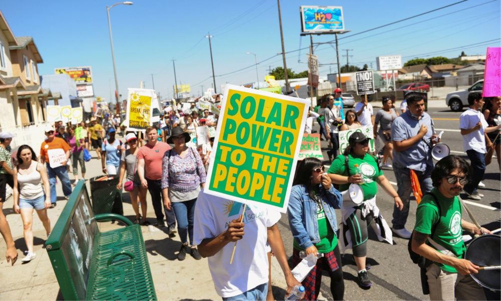 A person in the foreground carries a sign reading "Solar Power to the People" at a demonstration on the Pacific Coast highway during People's Climate March protest for the environment in the Wilmington neighborhood in Los Angeles, California. The march, which specifically protested the expansion of a Tesoro refinery, was held in a heavily industrialized neighborhood and was led by environmental leaders from indigenous and minority communities.