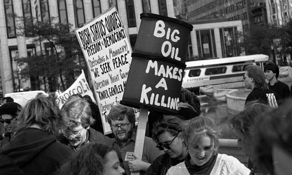 black-and-white photo of people on a New York City street holding signs, one of which reads "Big Oil Makes a Killing"