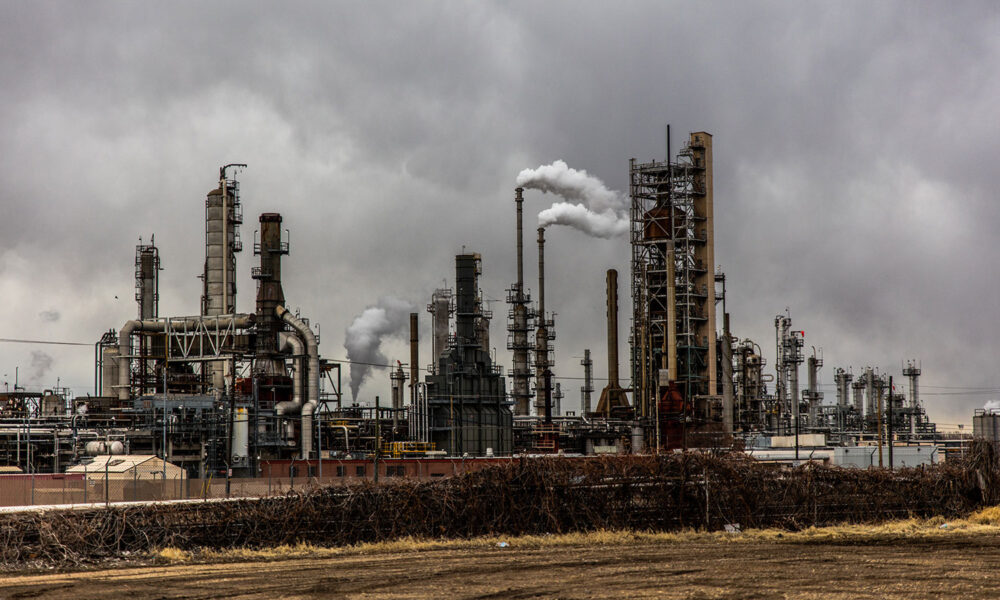 an oil refinery spews smoke into a gray sky
