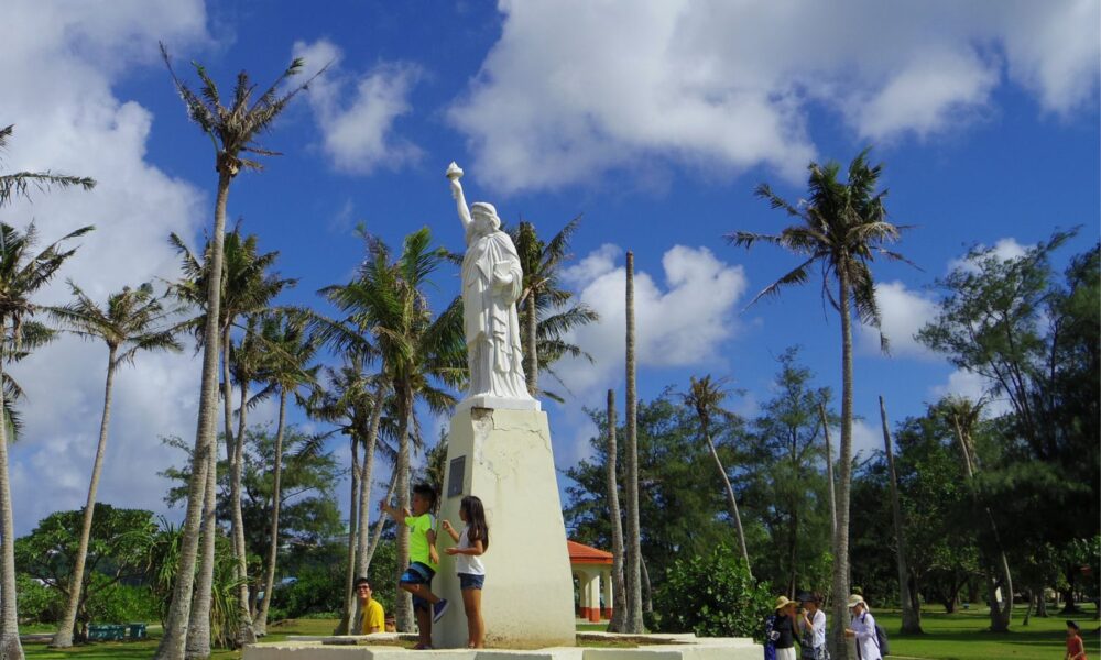 A couple of children stand in front of a scaled-down Statue of Liberty replica in Paseo Park in Hagatña, the capital of Guam, on a bright sunny day.
