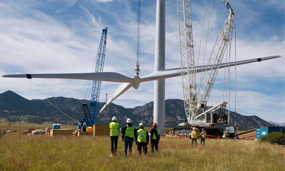 Workers watch installation of wind turbine blades.