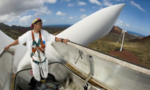 Man stands atop 110-foot high wind turbine.