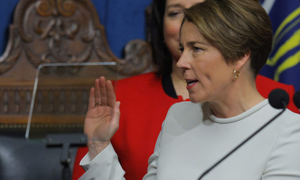 photo of Maura Healey behind a microphone and with her right hand raised to take the oath of office and become governor of Massachusetts