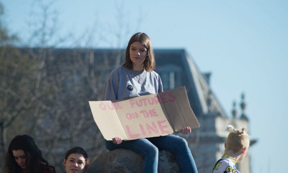 a young person holds a sign reading "Our future's on the line" at a protest