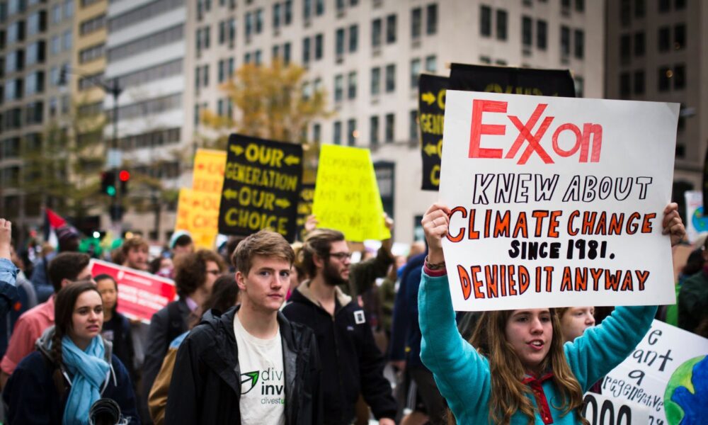a young protestor holds a sign reading "Exxon Knew about climate change since 1981 and denied it anyway"
