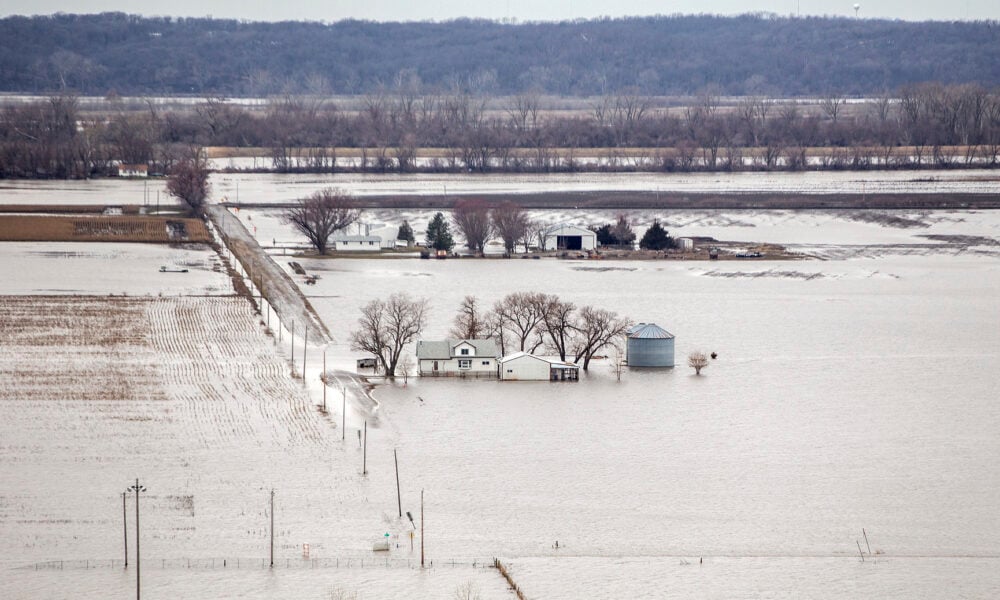aerial photo of a flooded farm; water is up to the sides of a farmhouse and silo, and a road next to the house is submerged