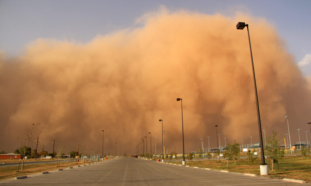photo of a massive wall of orange dust clouds moving down an empty road lined with tall streetlights, heading straight toward the camera
