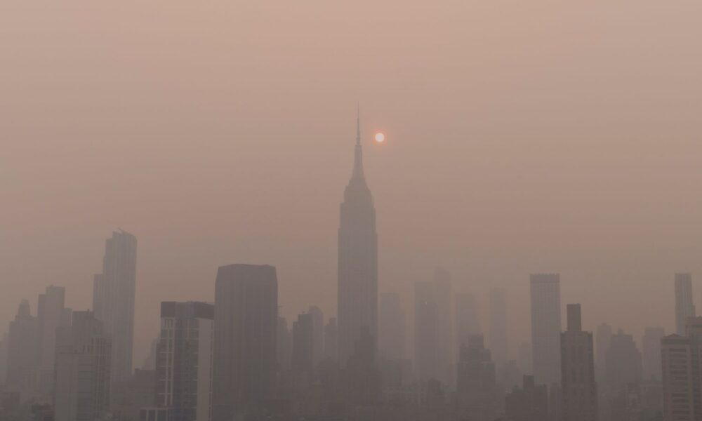 The New York City skyline at sunrise or sunset, with the sun and clear view of buildings obscured by yellowish haze from Canadian wildfires in June, 2023