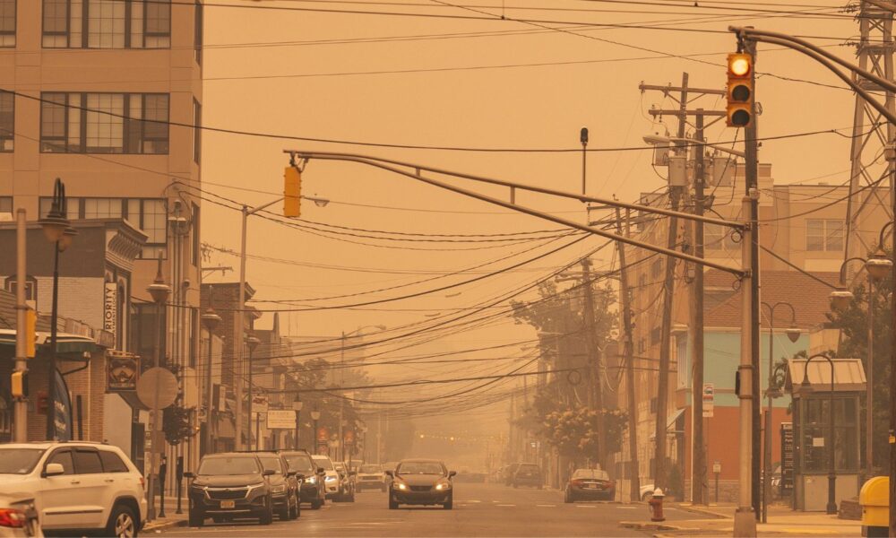 A street in Red Bank, NJ, with traffic lights and cars. Everything looks yellow and hazy because of smoke from the northern wildfires in the summer of 2023.