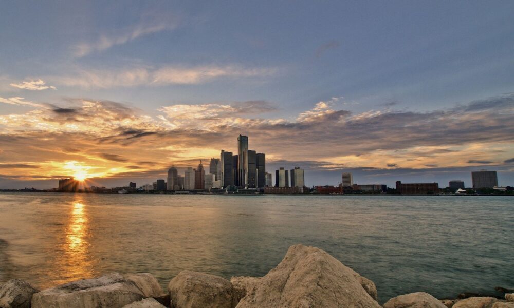 from the rocky shores of the Detroit River, the Detroit city skyline is pictured at sunrise