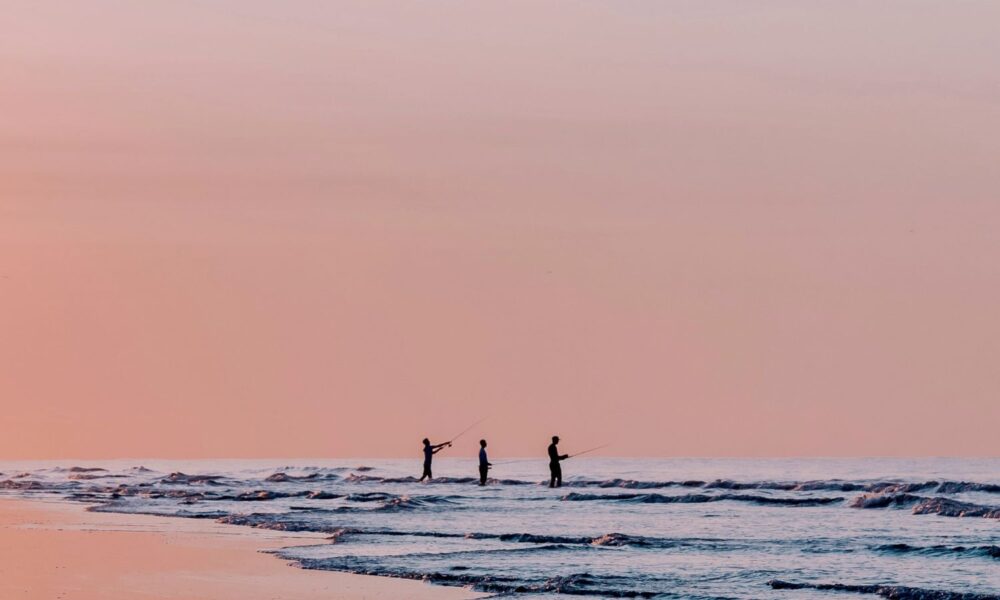 Silhouetted figures at sunrise or sunset are fishing in the ocean on Sullivan's Island, South Carolina.