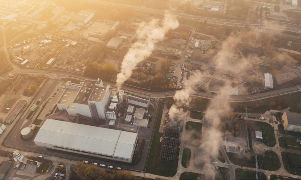 An aerial view of a neighborhood with the focus on an industrial facility spewing smoke into the air