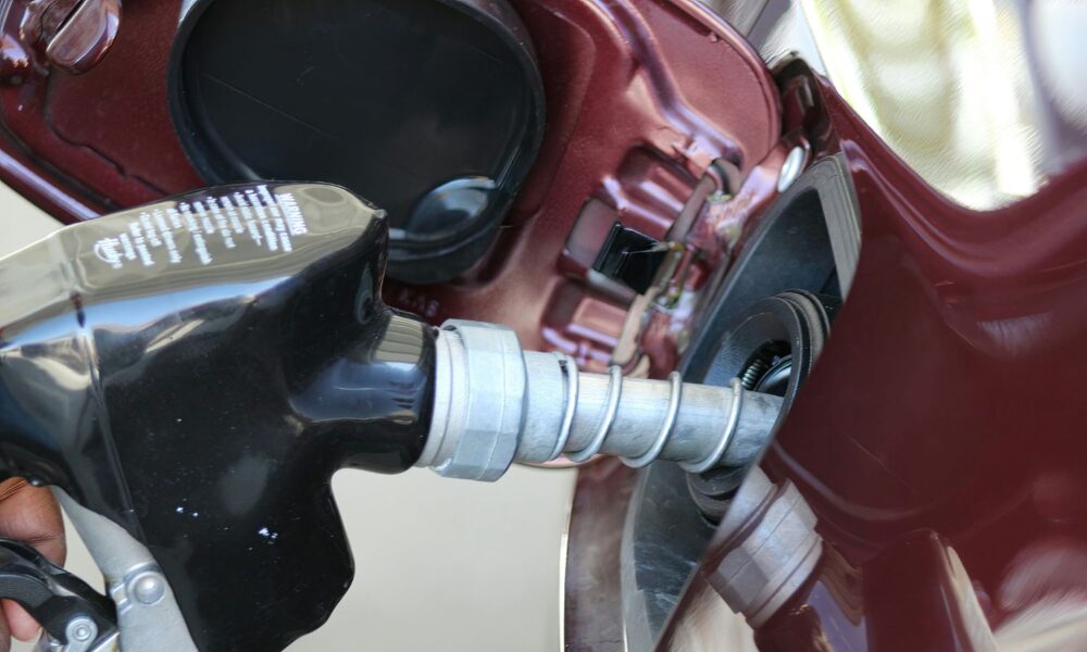 a close up of a person's hand holding a gas pump nozzle to a dark red car's fuel tank