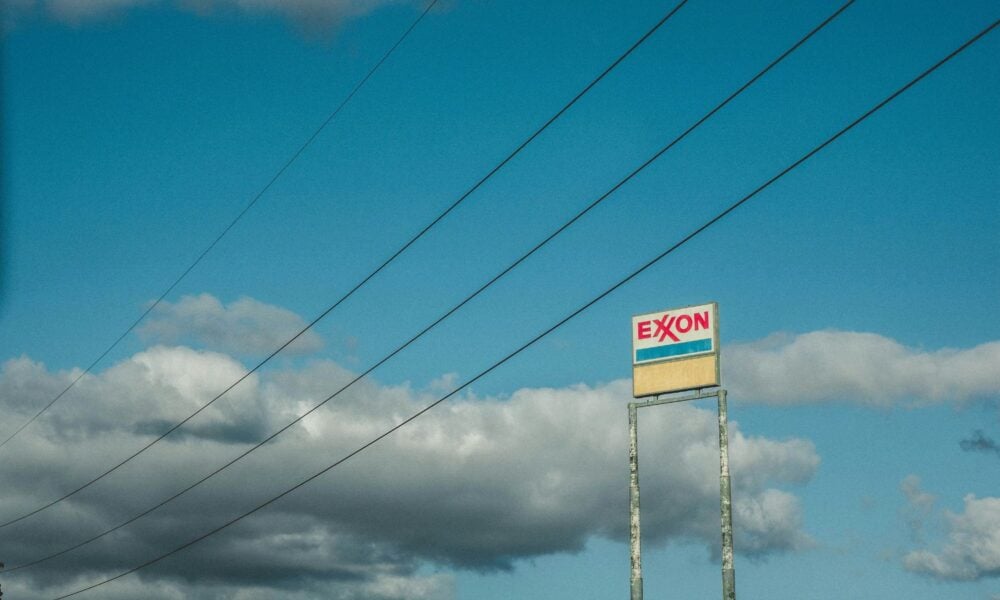 Old rusted Exxon sign against a cloudy blue sky, with wires sweeping the shot.