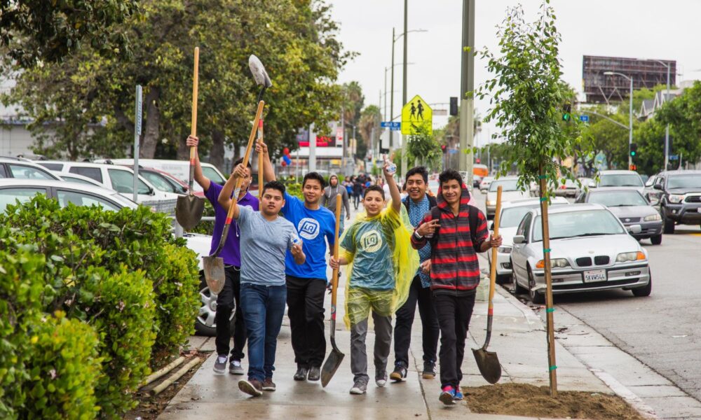 Students on their way to plant trees surrounding Manual Arts High School in South Los Angeles hold up their shovels as they walk down a sidewalk.