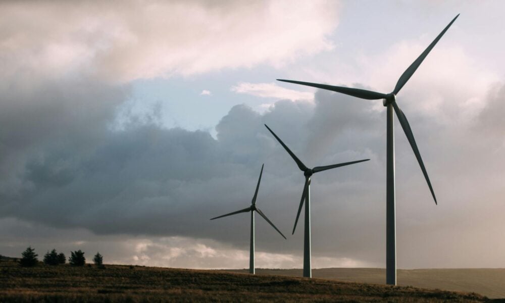 Three wind turbines are foregrounded against a moody, cloudy sky on a grassy plain