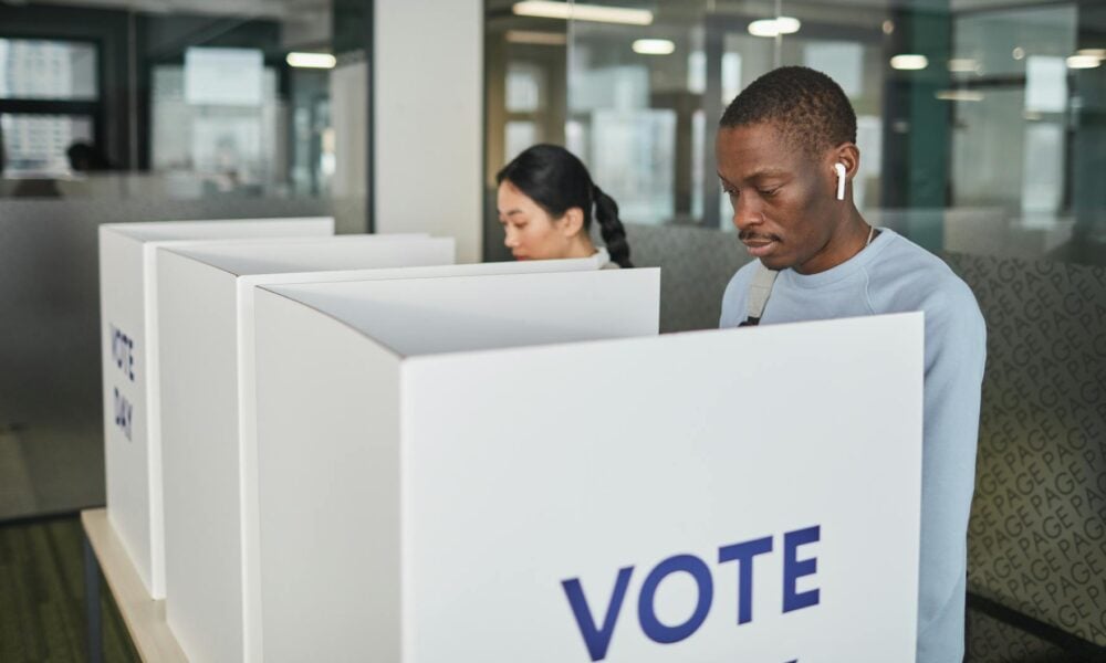 photo of two people standing side by side to fill out their ballots at separate voting booths