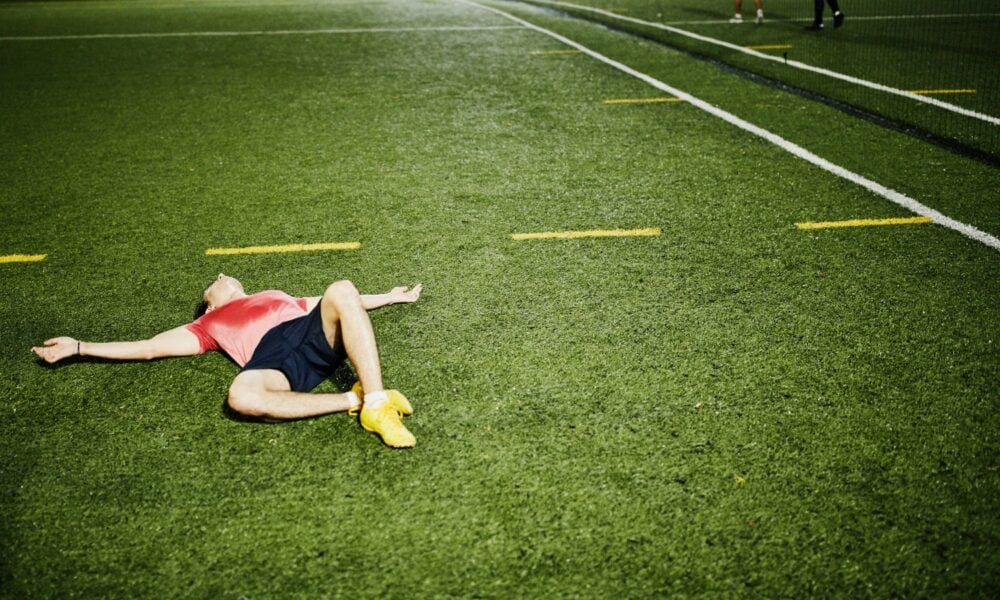 Exhausted male soccer player lying on field after evening soccer game.