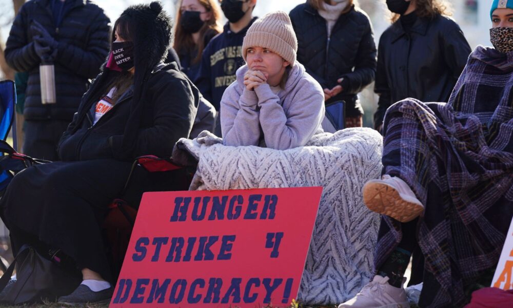 A coalition of conservative, progressive, and independent students, some over eight days into a hunger strike, congregate in front of the White House to urge President Biden to prioritize voting rights at Lafayette Park in December 2021 in Washington, DC. Centered is a young person holding a sign that reads Hunger Strike 4 Democracy!