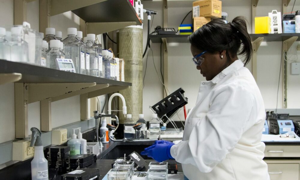 A woman in a scientific laboratory, wearing a lab coat and gloves.