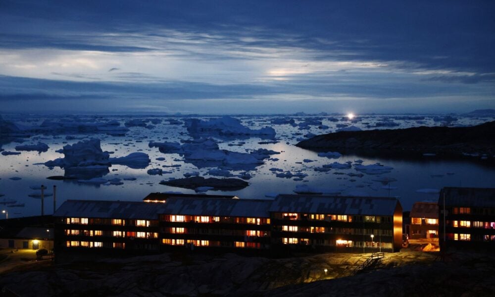 Icebergs float in Disko Bay, near a row of warmly illuminated houses, as moonlight shines through the clouds on September 03, 2021 in Ilulissat, Greenland.