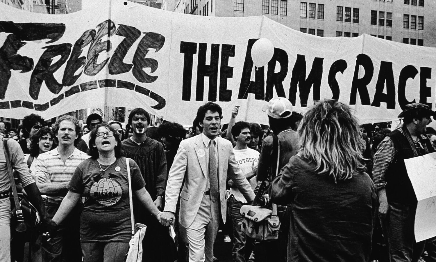 black and white photo of demonstrators marching hand in hand in New York City in 1982, under a large banner reading "Freeze the arms race"