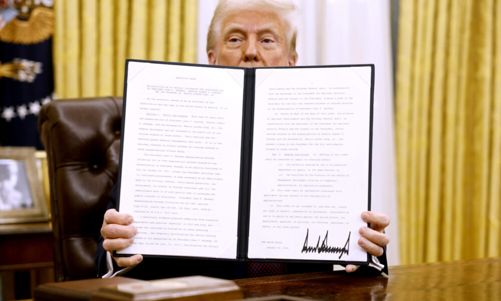 President Trump sits in the Oval Office and holds up an executive order.