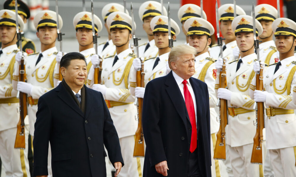 US President Trump and Chinese President Xi Jinping walk past rows of Chinese soldiers standing at attention holding rifles and wearing dress white uniforms